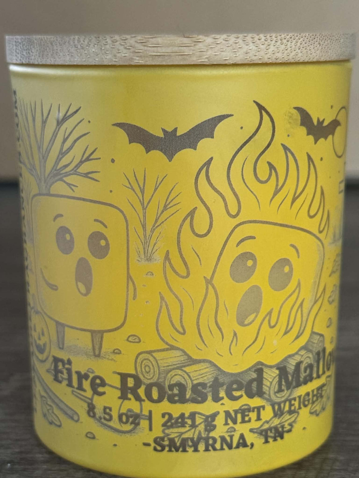 Fire Roasted Mallow soy candle front view with yellow campfire character jar