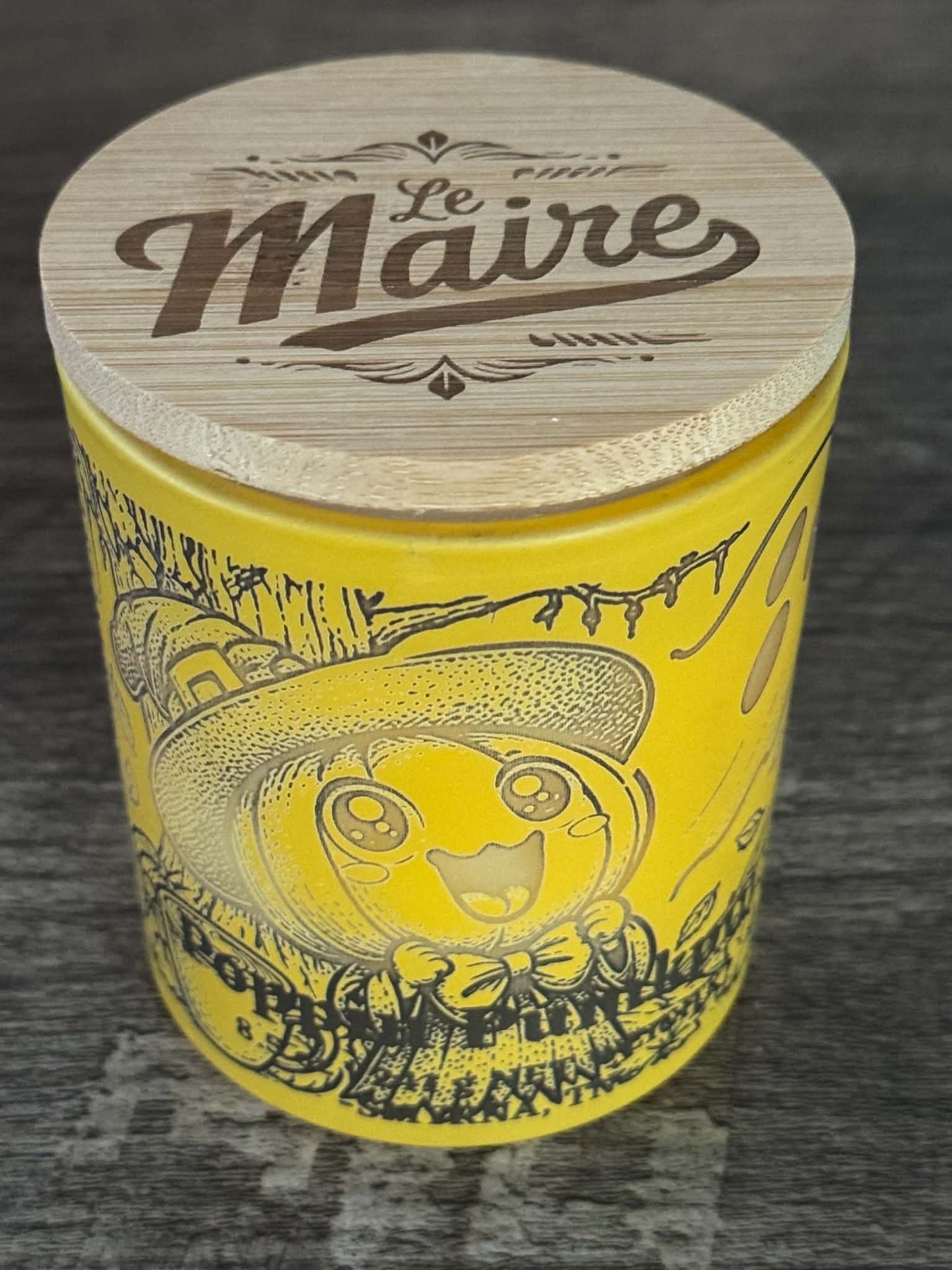 Poppin Pumpkin soy candle angled view in yellow character jar with Le Maire wood lid