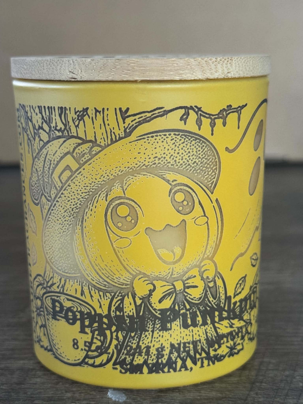 Poppin Pumpkin soy candle front view in yellow character jar with Le Maire wood lid